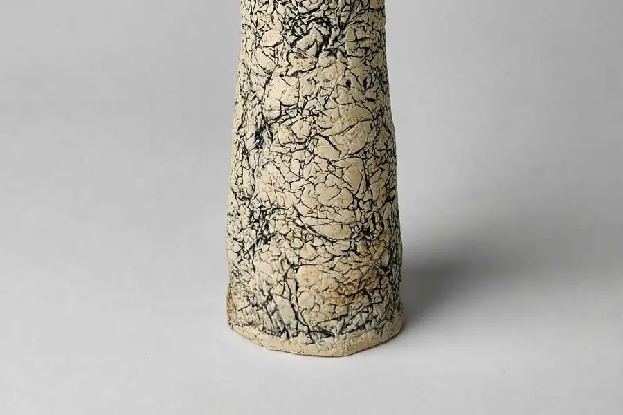 Close-up of a tall ceramic vessel with a crackled black-veined ivory glaze